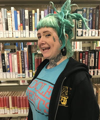 Heather Krieger; woman with blue hair in front of a bookshelf