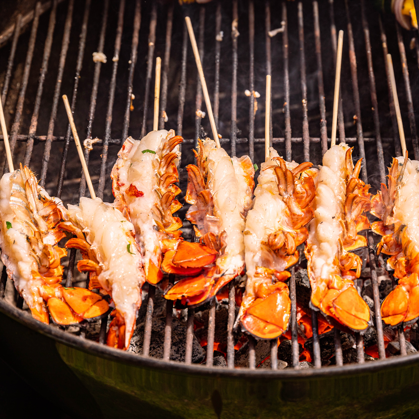 Load image into Gallery viewer, Split Lobster Tails on grill with skewer
