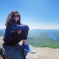 Cassandra Johnson; woman sitting on a rock on the summit of a mountain.