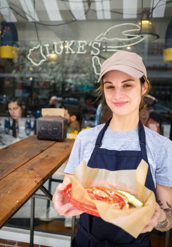 Woman standing in Front of a Luke's Lobster Shack holding a basket with a lobster roll