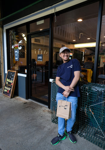 A smiling person holding a Luke's Lobster takeout bag standing in front of decorative lobster crates