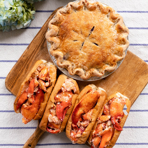 Lobster rolls and a pie on a wooden board with hydrangeas in the background