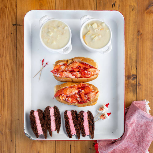 Tray with lobster rolls and side dishes on a wooden surface