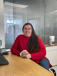 Tracy Carp smiling while sitting at a desk wearing a red sweater