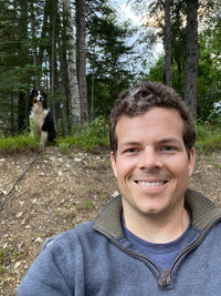 Selfi of Chris Jordan in the woods with a dog in the background
