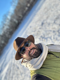 Person wearing a hat and sunglasses with a snowy landscape in the background