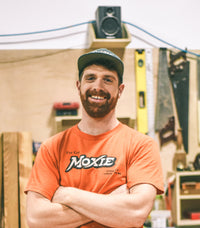Nate wearing a orange Moxie tee posing for a photo in the woodshop