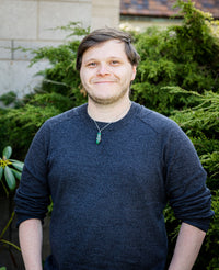 Matthew posing for a picture outside while wearing a blue sweater