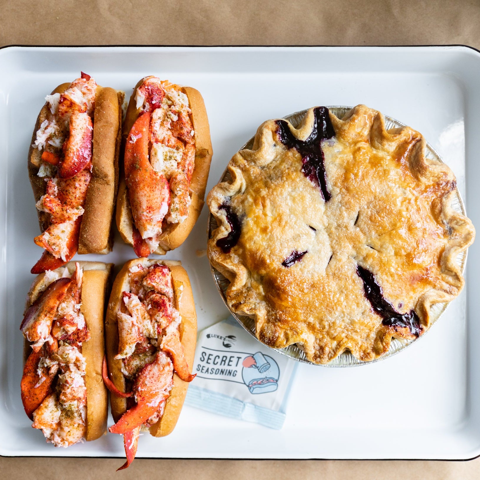 Load image into Gallery viewer, Four lobster rolls and a berry pie on a white tray with a brown background
