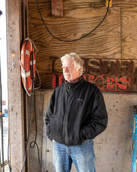 Jeff Holden smiling and looking off into the distance while wearing a black jacket and blue jeans