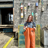 Emmaline posing in front of a buoy wall while wearing orange Grundens