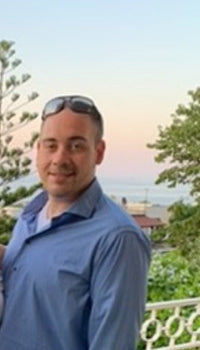 Damian wearing a blue button down shirt and sunglasses posing for a picture outside