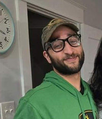 Joe wearing a baseball hat, glasses, and a green sweatshirt posing for a photo
