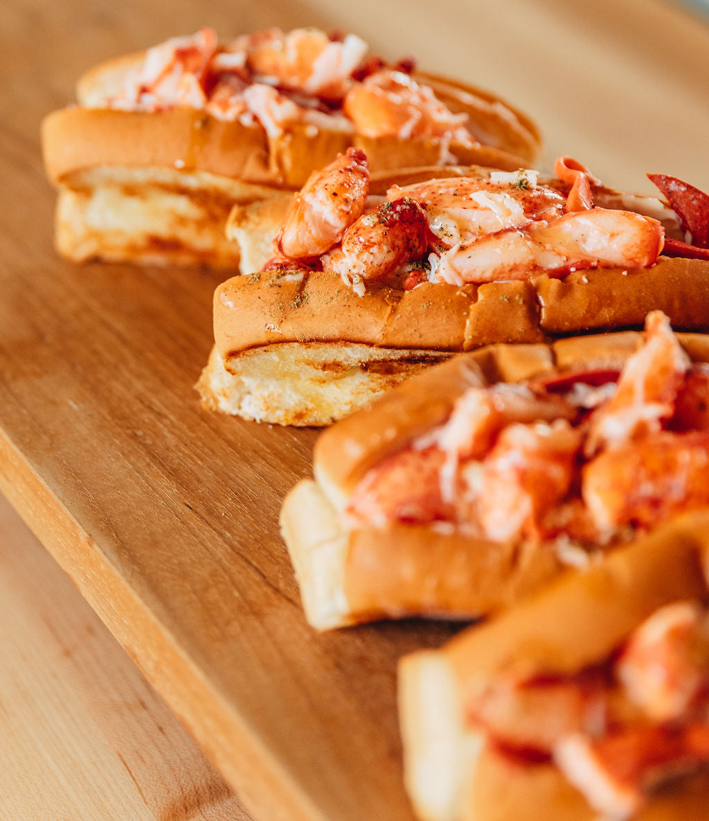Load image into Gallery viewer, close up of four lobster rolls on a wooden tray
